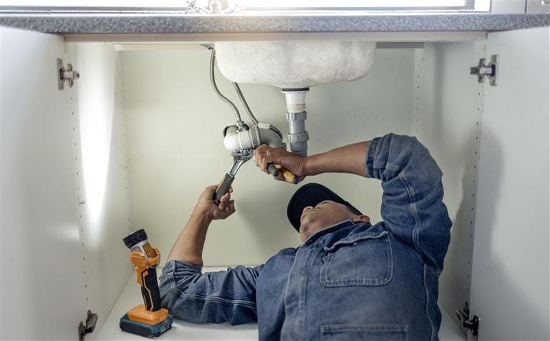 Plumber repairing pipes beneath a bathroom sink in Titusville