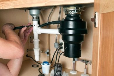 Plumber repairing a garbage disposal beneath a kitchen sink in Titusville